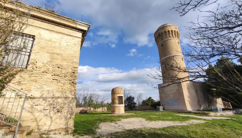 Torri antiche e un piccolo edificio circolare nel parco del cardeto, sotto un cielo azzurro con nuvole bianche.