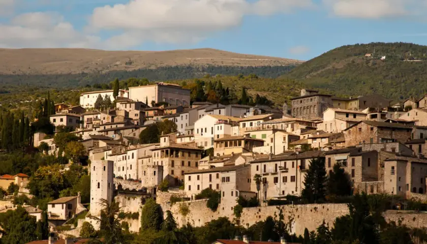 Spello, un borgo umbro incastonato tra colline verdi, con case in pietra e torri antiche che si stagliano contro il cielo azzurro.