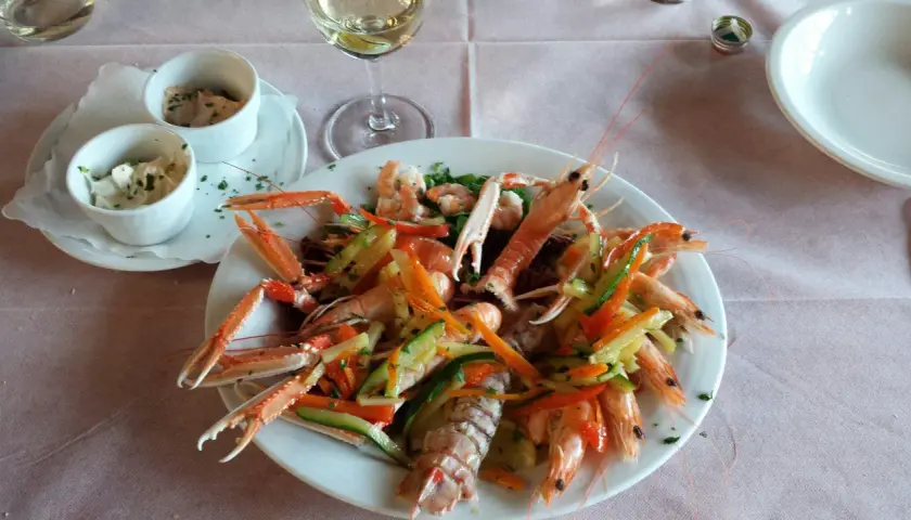 Un piatto di scampi e gamberi con verdure miste, un bicchiere di vino bianco e salse, un'ottima cena al conte Max Monte Roberto.