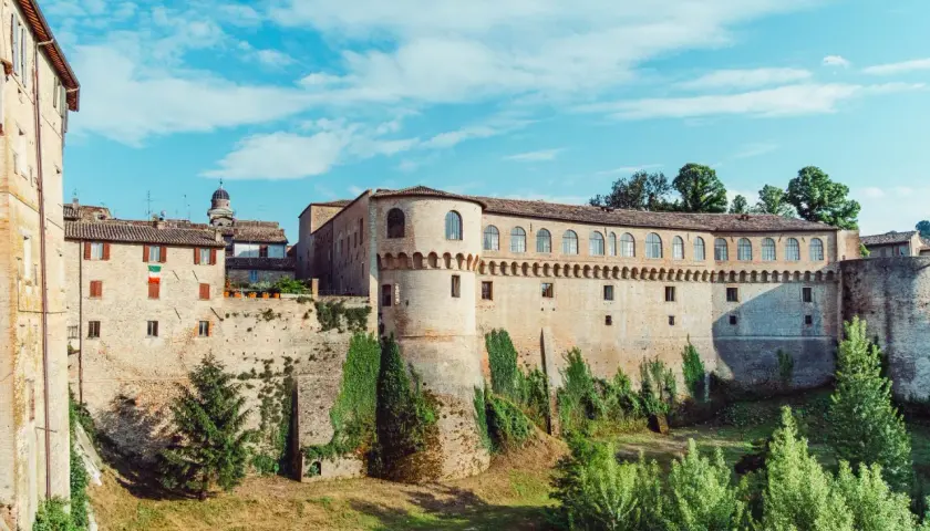 Un imponente palazzo storico con torri e mura di mattoni, circondato da vegetazione. Un luogo da scoprire: Urbania cosa vedere.