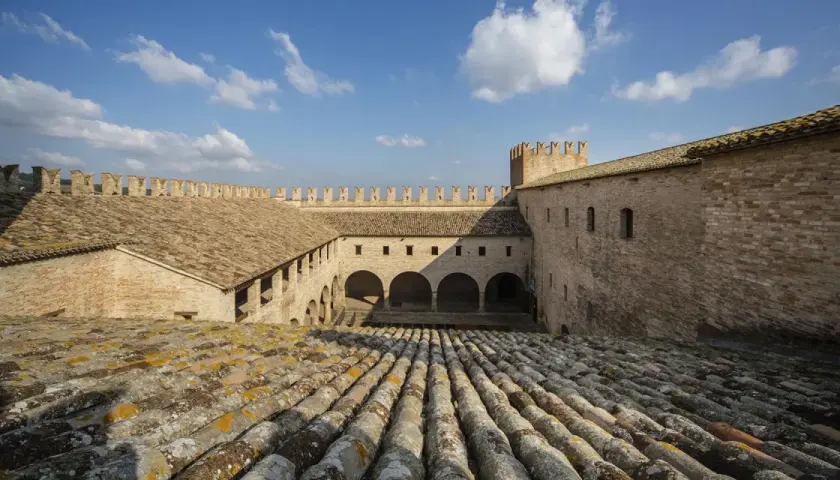 Cortile interno di un castello a Tolentino, Marche, con tetti in cotto e cielo azzurro.