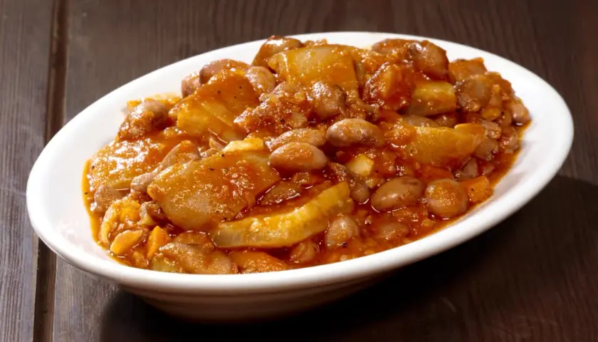 Piatto fumante di fagioli con le cotiche, un classico della ricetta marchigiana, servito in una ciotola bianca su un tavolo di legno scuro.