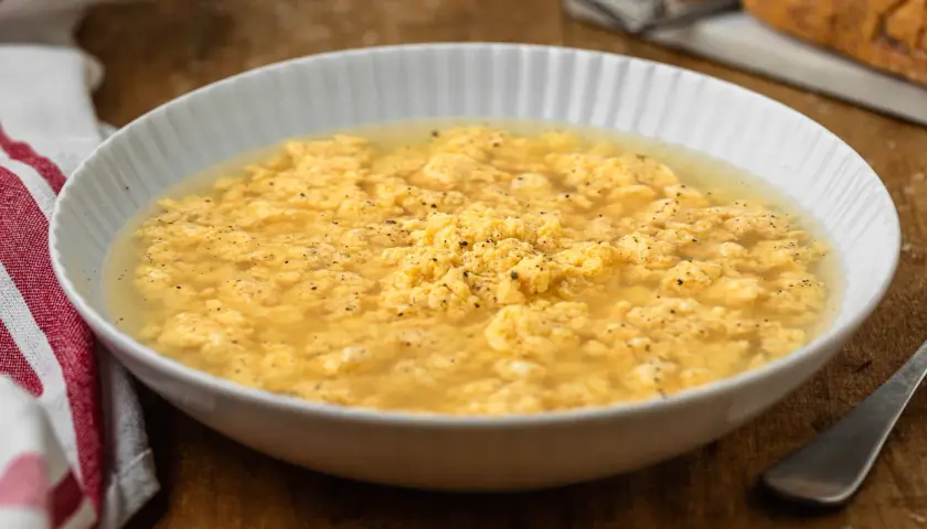 Stracciatella in brodo marchigiana, un piatto confortante con uova strapazzate in brodo, pepe nero e un tocco di formaggio grattugiato.