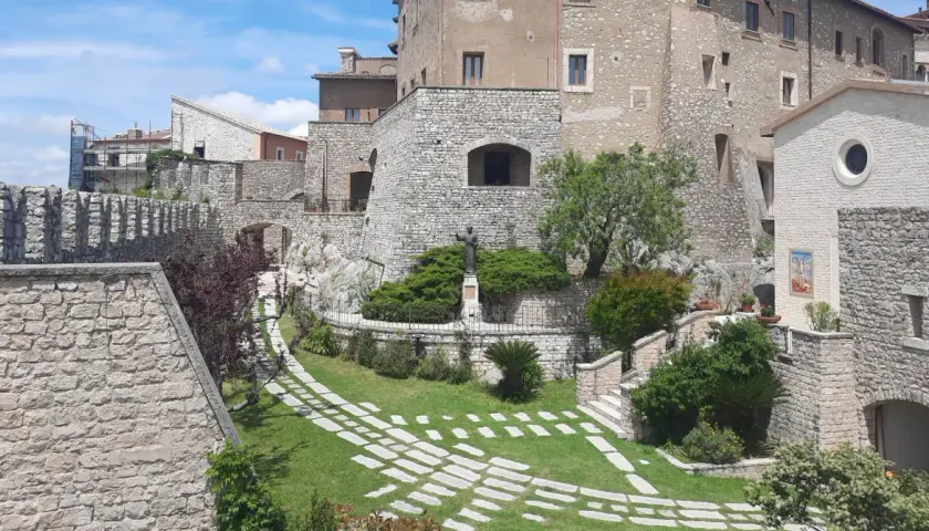 Un angolo suggestivo del centro storico di Rieti, con antiche mura in pietra, un giardino curato e una statua.