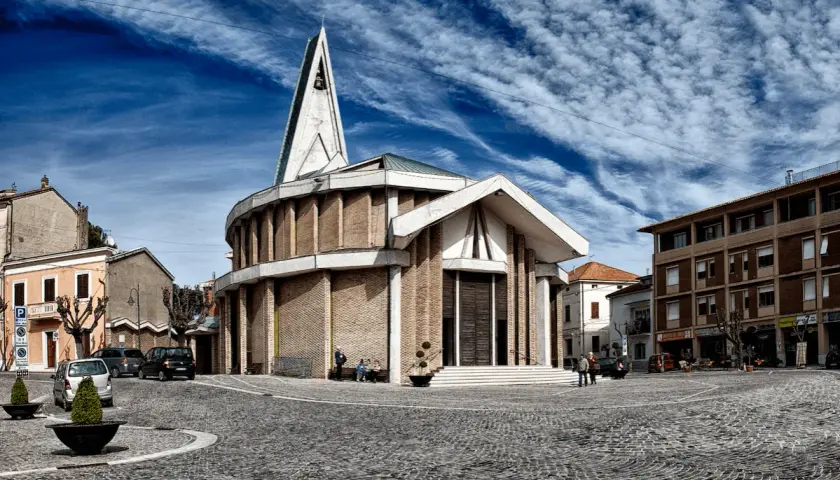 Piazza del centro di Numana con una chiesa moderna, cielo blu e nuvole bianche.