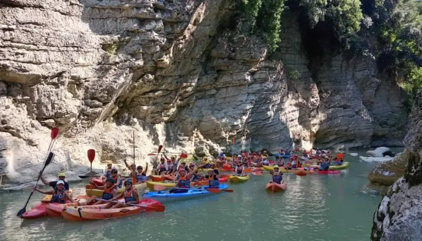 Gente in kayak esplora un canyon con pareti rocciose imponenti, simili a marmitte dei giganti nelle Marche.