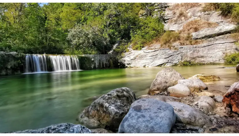 Le cascatelle di Castel Trosino creano un'oasi verde smeraldo, con rocce levigate e vegetazione lussureggiante.