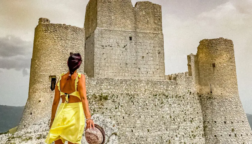 Donna in abito giallo ammira la Rocca Calascio, un luogo da non perdere per la sua storia e panorami mozzafiato.