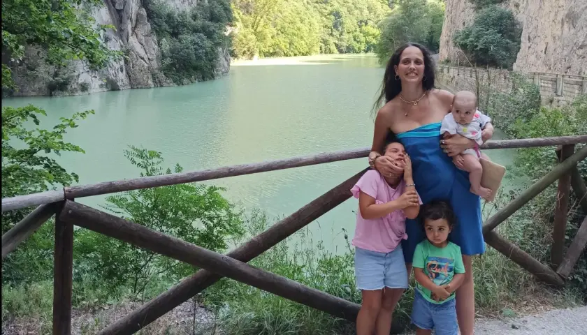 Famiglia felice nella golena del Furlo, con un lago turchese e montagne verdi sullo sfondo.