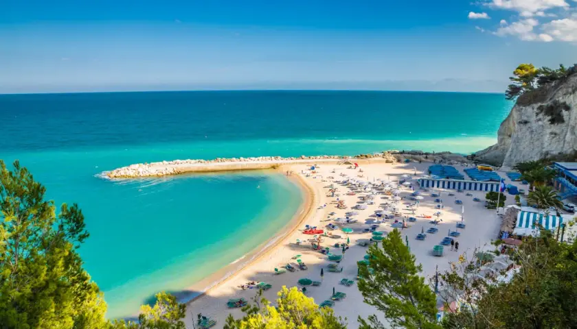 Spiagge Sirolo con acque turchesi, sabbia dorata, ombrelloni e gente che si gode il sole.