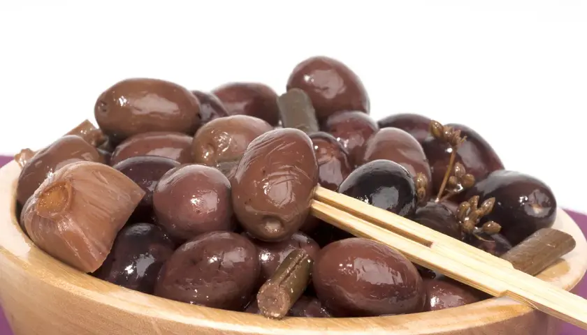 Olive nere sotto sale, un assaggio della ricetta marchigiana. Un piatto di olive scure e lucide in una ciotola di legno.
