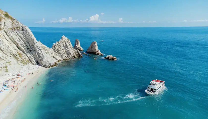 La spiaggia delle Due Sorelle, con le sue iconiche rocce, accoglie bagnanti e kayak. Una barca solca il mare azzurro.