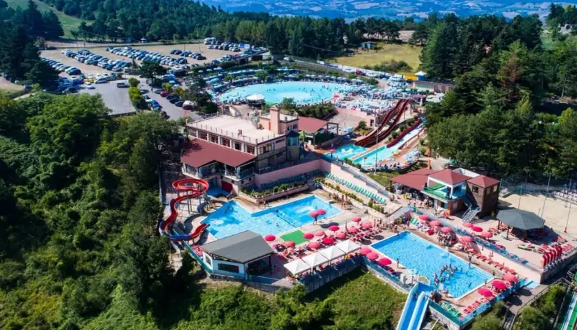 Vasta area con piscine, scivoli e ombrelloni rossi, immersa nel verde delle colline. Un divertente parco acquatico nelle Marche per tutta la famiglia.