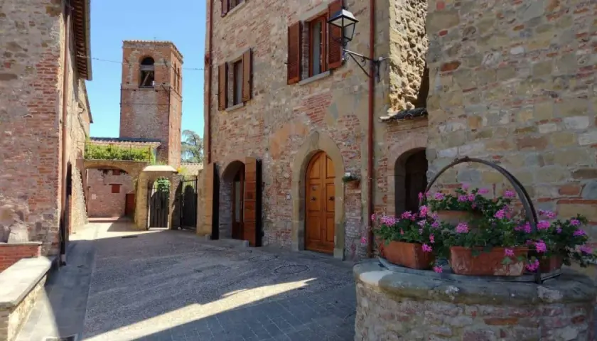 Un vicolo in pietra con un pozzo fiorito e un campanile sullo sfondo. Citerna cosa vedere: un borgo medievale incantevole.