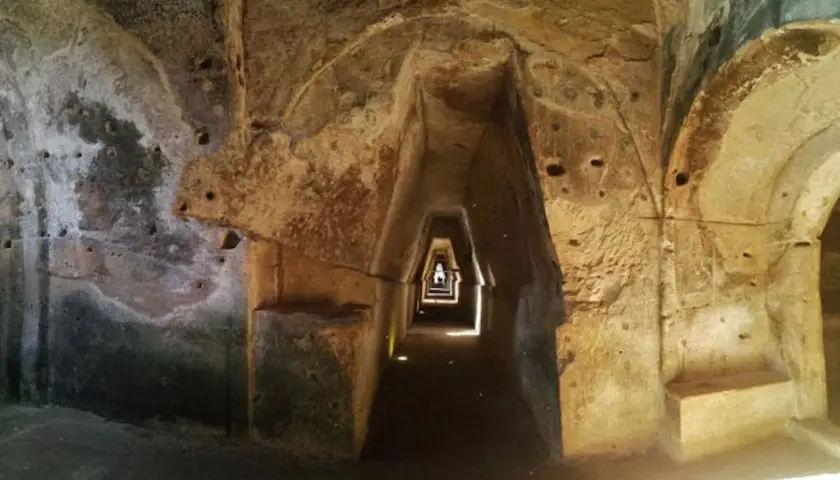 Interno della grotta della Sibilla: un corridoio stretto e trapezoidale scavato nella roccia, con nicchie e aperture.