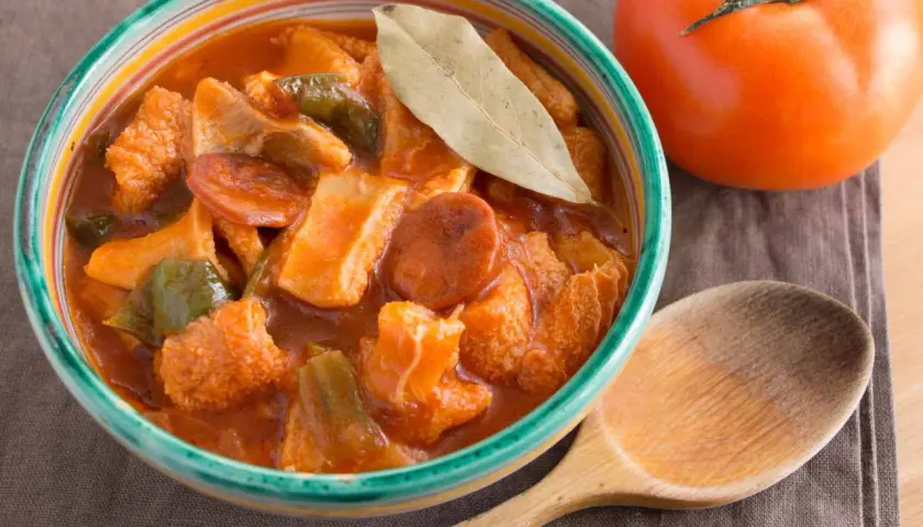 Un invitante piatto di trippa alla marchigiana, con peperoni e pomodoro, pronto per essere gustato con un cucchiaio di legno.