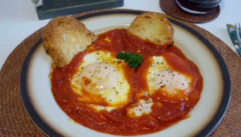 Uova in trippa marchigiana, un piatto saporito con uova in camicia su un letto di sugo rosso, guarnito con pane tostato e prezzemolo.