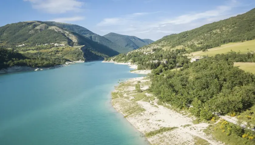 Spiaggia libera sul lago di Fiastra, con acque turchesi e montagne verdi sullo sfondo. Un luogo ideale per rilassarsi e godersi la natura.