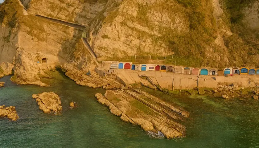 Piccole casette colorate a ridosso della scogliera, con il mare verde smeraldo che lambisce le rocce. Un angolo di paradiso vicino alla grotta azzurra di Ancona.