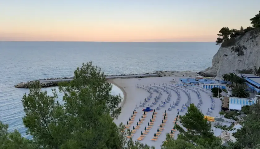 Spiaggia ordinata con lettini e ombrelloni, ideale per scoprire cosa vedere a Numana e Sirolo. Mare calmo al tramonto.