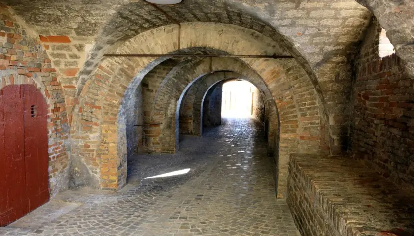 Arco in mattoni a Corinaldo, cosa vedere: un suggestivo passaggio coperto con pavimentazione in pietra e una porta rossa.
