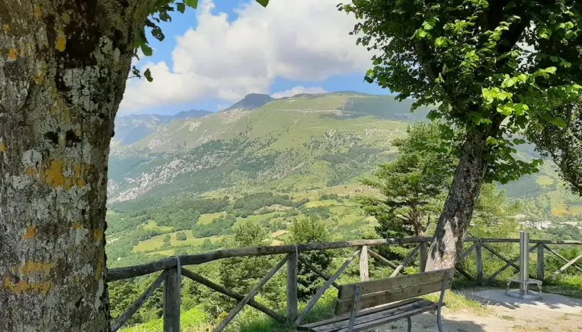 Panoramica mozzafiato del monte Monaco nelle Marche, con un sentiero serpeggiante e un cielo azzurro con nuvole bianche.