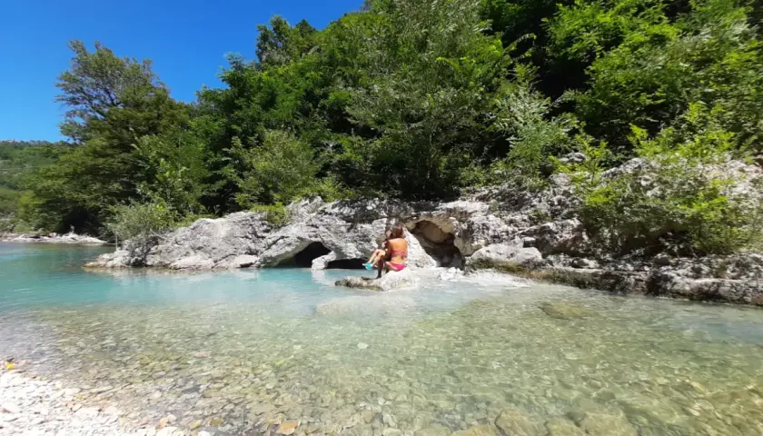 Bambini giocano nel **genga fiume** dalle acque cristalline, circondato da rocce e vegetazione lussureggiante.