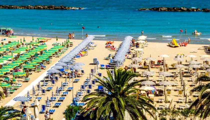 San Benedetto del Tronto: un'ampia spiaggia dorata con file ordinate di ombrelloni verdi e bianchi, lettini e palme. Il mare pulito invita al relax.