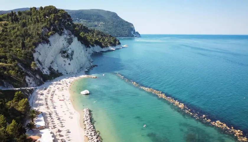 Spiaggia affollata con ombrelloni e lettini, scogliere bianche e mare azzurro a Porto Sant'Elpidio Mare.