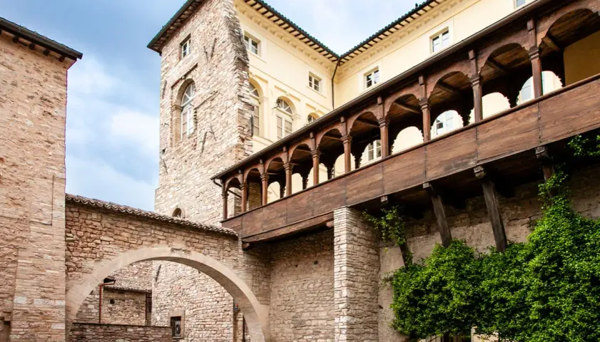 Cortile storico con archi in pietra e un loggiato in legno. Un assaggio di cosa vedere a Spello in un giorno, tra storia e natura.