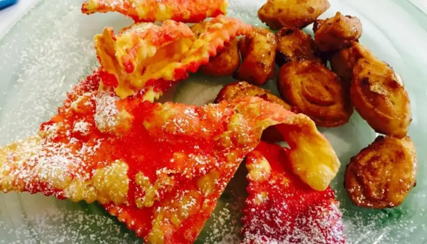 Cresciole marchigiane di Benedetta, dolci fritti cosparsi di zucchero a velo, con un tocco di rosso vivace.