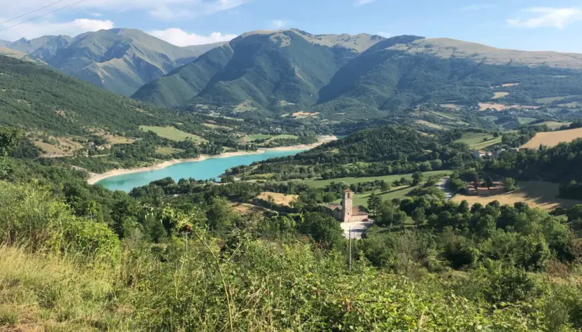Panoramica del lago di Fiastra, con montagne verdi, un borgo e una chiesa. Cosa vedere in questo paesaggio mozzafiato.