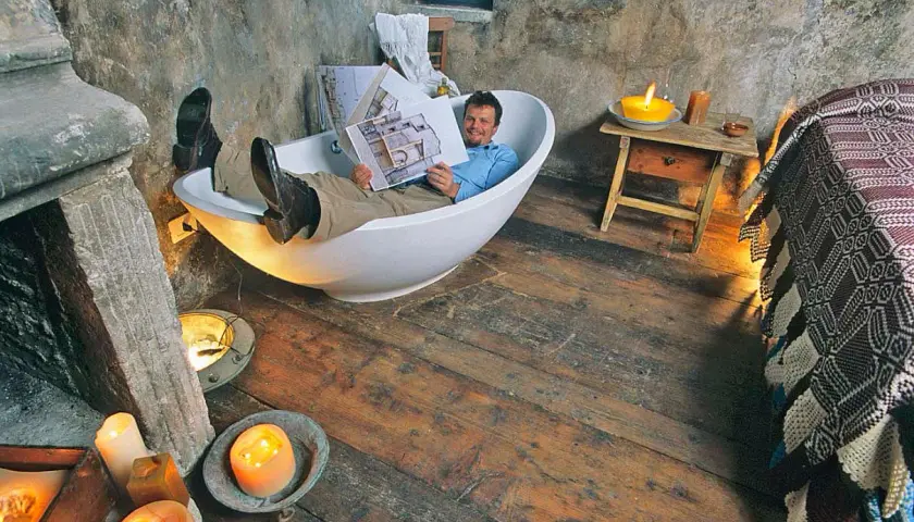 Uomo rilassato in vasca da bagno, legge un libro in un ambiente rustico, forse una casa vacanze a Santo Stefano, Abruzzo, con candele accese.