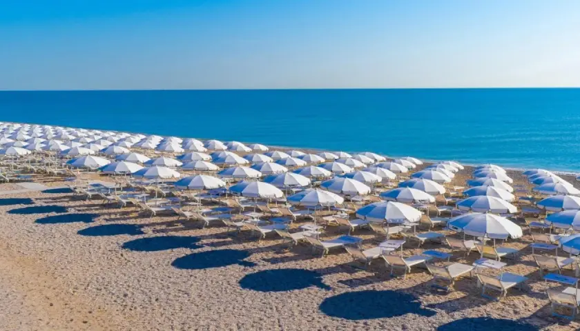 Filettate file di ombrelloni bianchi e lettini sulla spiaggia di Porto San Elpidio, con il mare azzurro sullo sfondo.