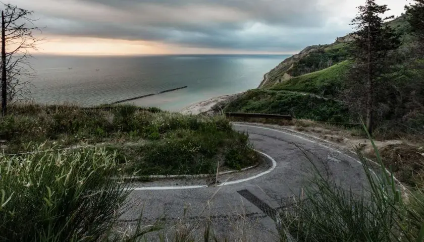 Strada panoramica che sale verso il tetto del mondo a Pesaro, con vista sul mare Adriatico e una costa verdeggiante.