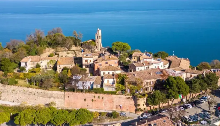Borgo medievale di Gabicce Mare cosa vedere: un incantevole panorama di case con tetti rossi, un campanile e il blu del mare Adriatico.