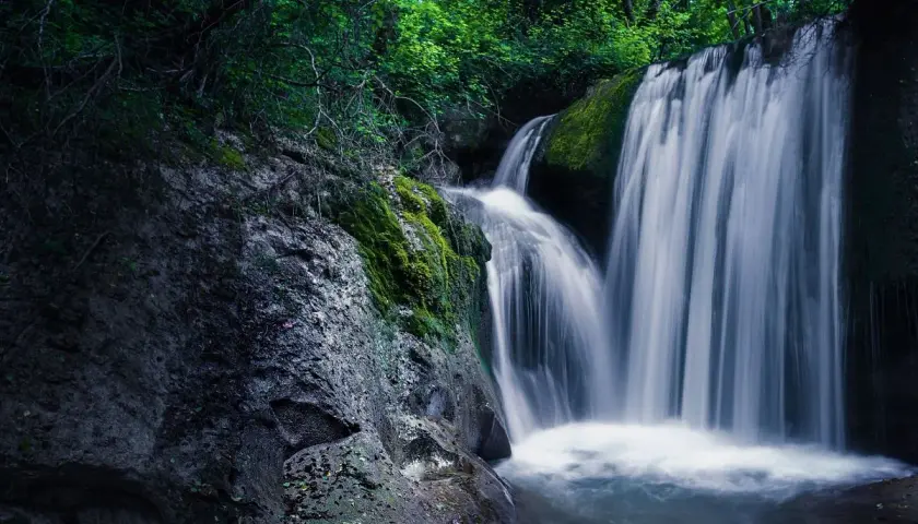 Cascate nelle Marche, un'oasi di pace tra rocce muschiose e vegetazione rigogliosa. L'acqua scende impetuosa, creando un velo bianco e setoso.
