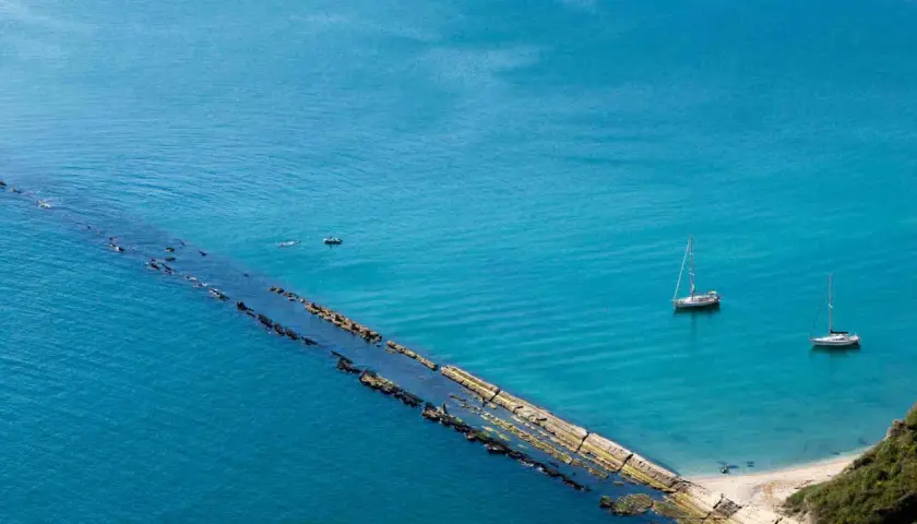 La spiaggia del Trave, con le sue acque cristalline, ospita due barche a vela e un piccolo motoscafo.
