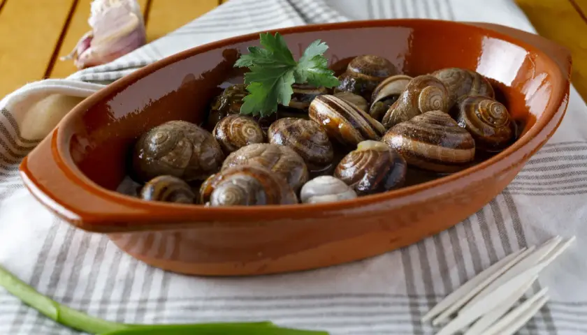 Lumachine di mare in porchetta, un piatto gustoso servito in una ciotola di terracotta con aglio e prezzemolo.