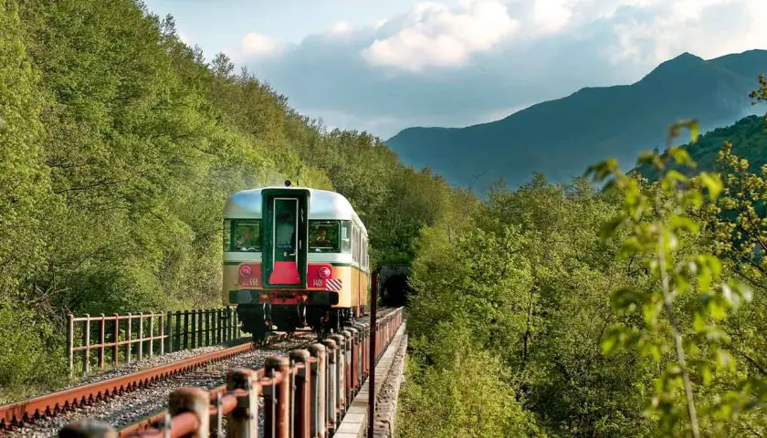Treno d'epoca attraversa un viadotto immerso nel verde, tra Fabriano e Ancona, dirigendosi verso un tunnel tra le montagne.