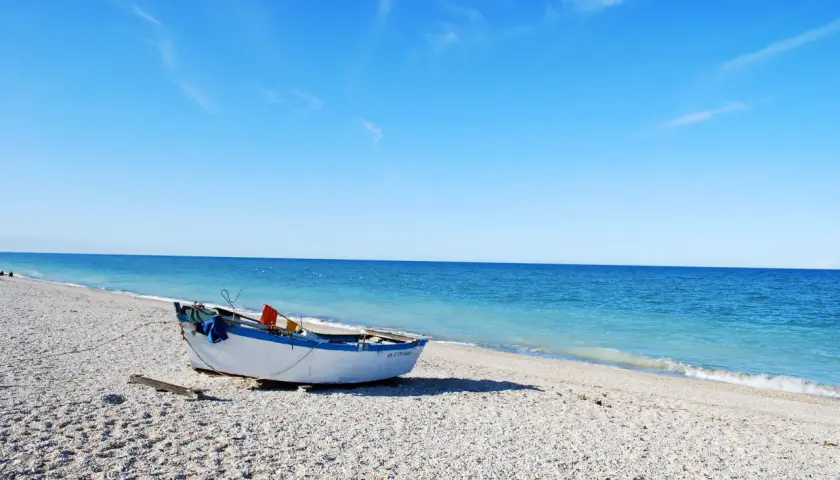 Barca bianca e blu sulla spiaggia di ciottoli a Senigallia, mare calmo e cielo azzurro.