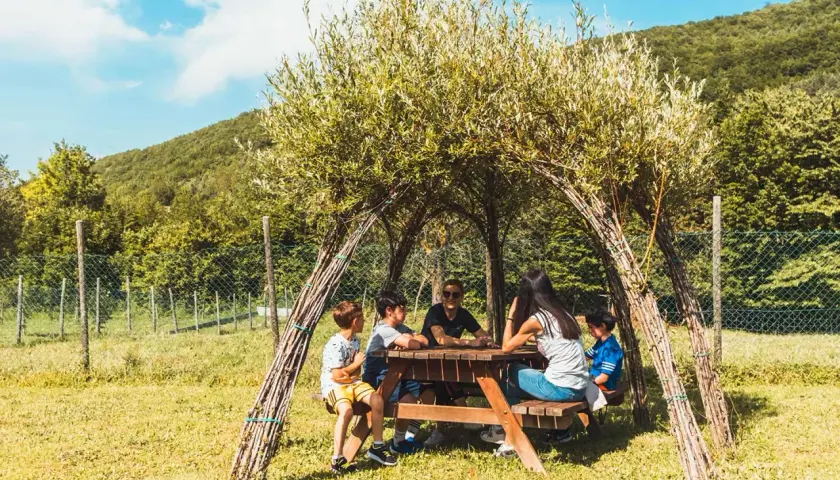Bambini riuniti attorno a un tavolo da picnic sotto una tettoia naturale nel bosco dei folletti Urbania.