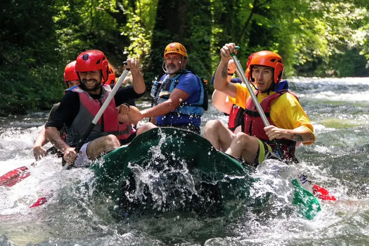 Un gruppo di amici si diverte in un'avventura di rafting nelle Marche, pagaiando con entusiasmo tra le rapide.