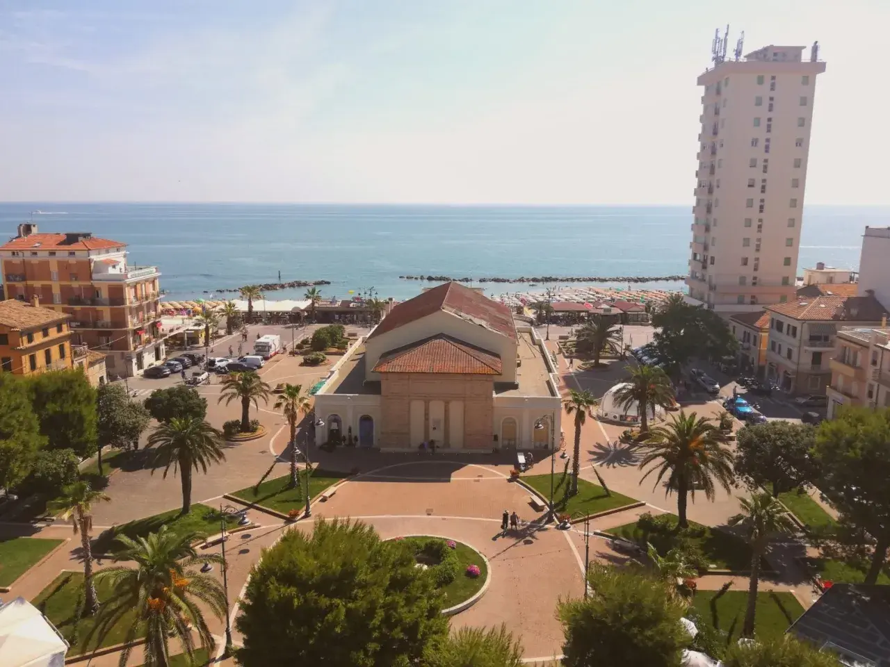 Piazza centrale con teatro, palazzi, palme e mare sullo sfondo. Ecco cosa vedere a Porto Recanati.