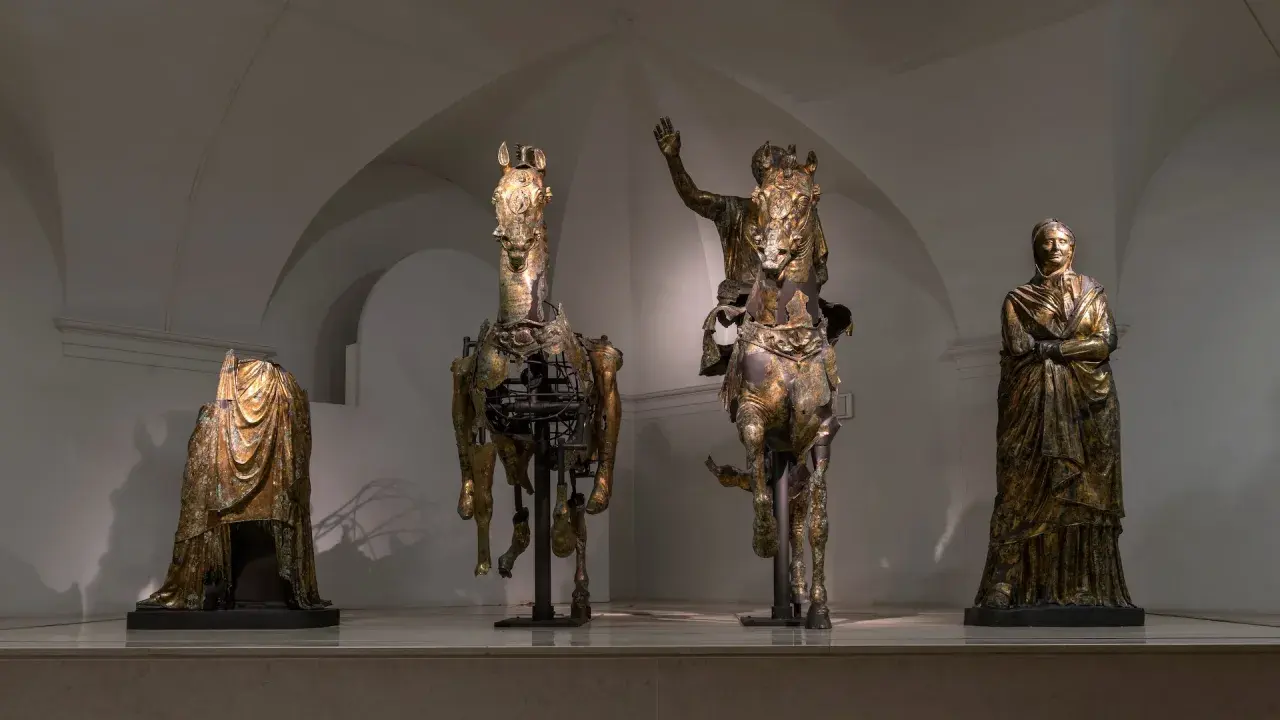 Statue equestri e figure umane in bronzo dorato, un'antica **pergola** che evoca le Marche.