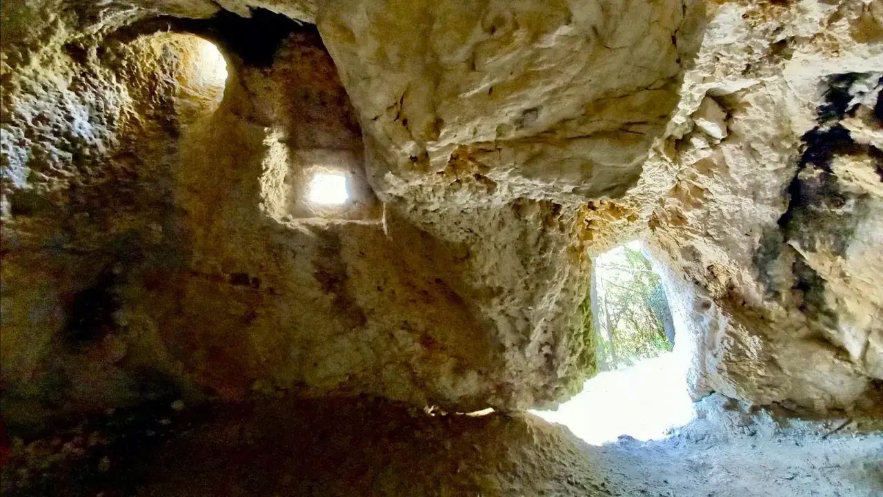Interno della grotta del mortarolo, con aperture che illuminano le rocce calcaree e un'uscita verso il verde.