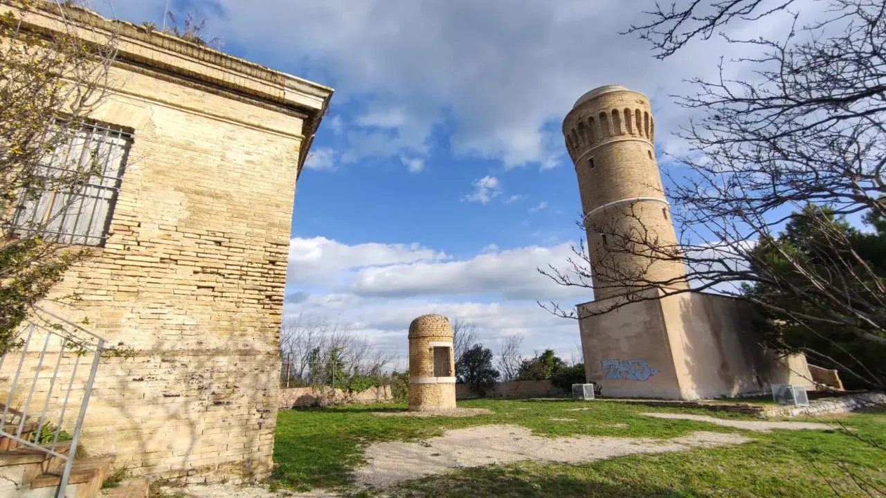 Torri antiche e un piccolo edificio circolare nel parco del cardeto, sotto un cielo azzurro con nuvole bianche.