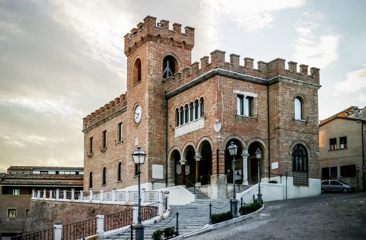 Edificio storico in mattoni a Mondolfo, cosa vedere: torre con orologio, archi e scalinata.