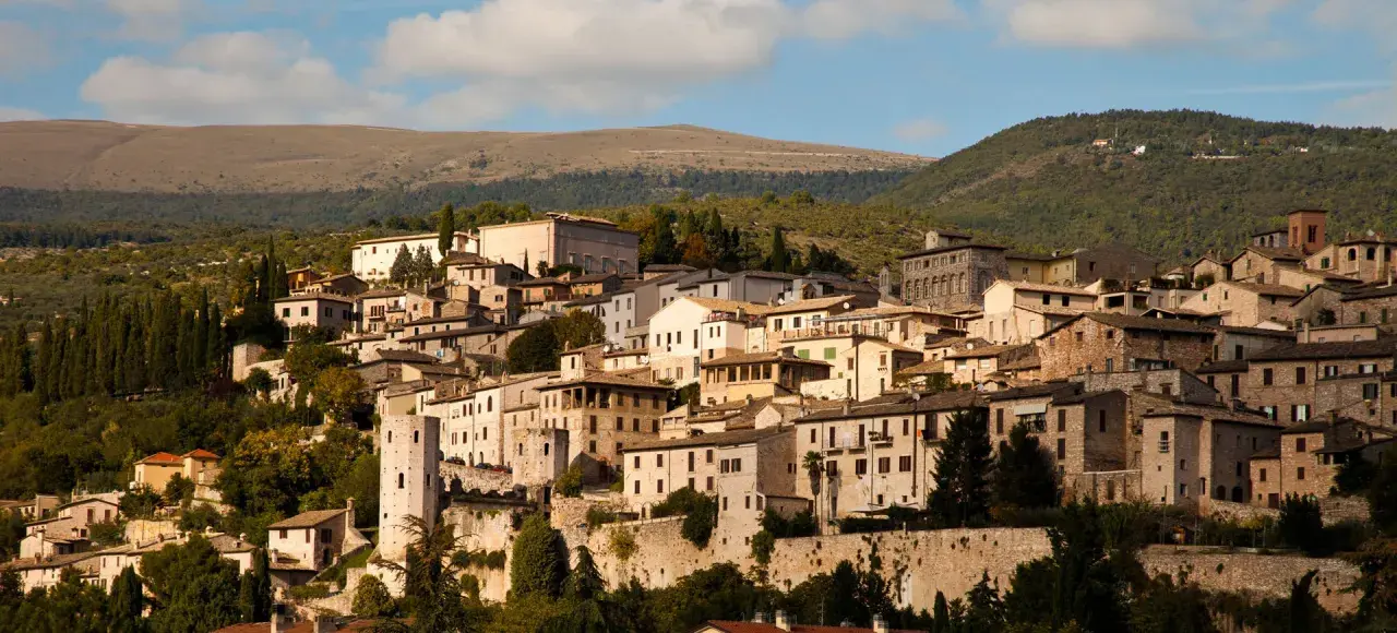 Spello, un borgo umbro incastonato tra colline verdi, con case in pietra e torri antiche che si stagliano contro il cielo azzurro.