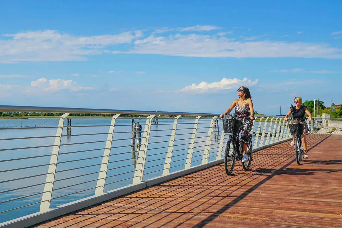 Due donne in bicicletta su una moderna pista ciclabile jesi, con il mare e il cielo azzurro sullo sfondo.